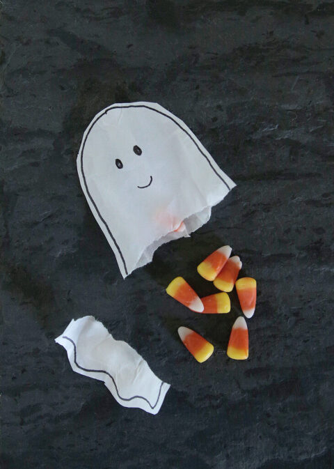 paper ghost treat bag ripped open with candy corn spilling from bag