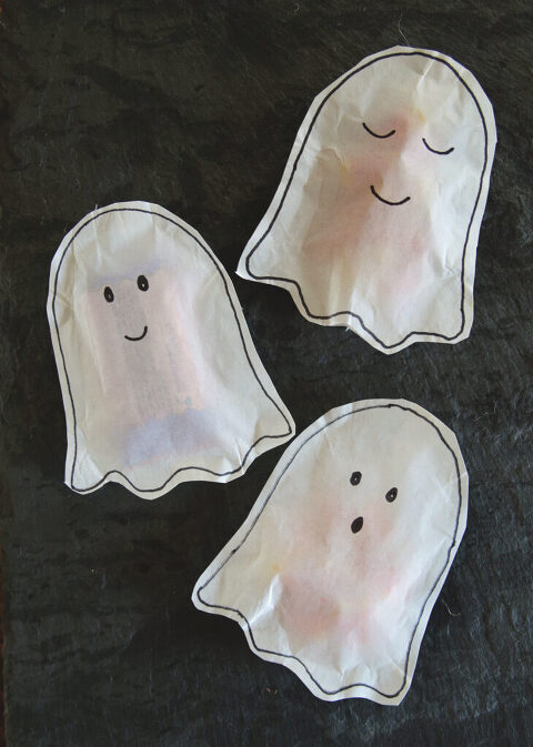 three white paper ghost treat bags on dark gray stone