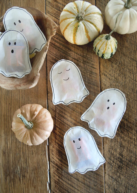 white paper ghost treat bags laying on wood table with small pumpkins surrounding