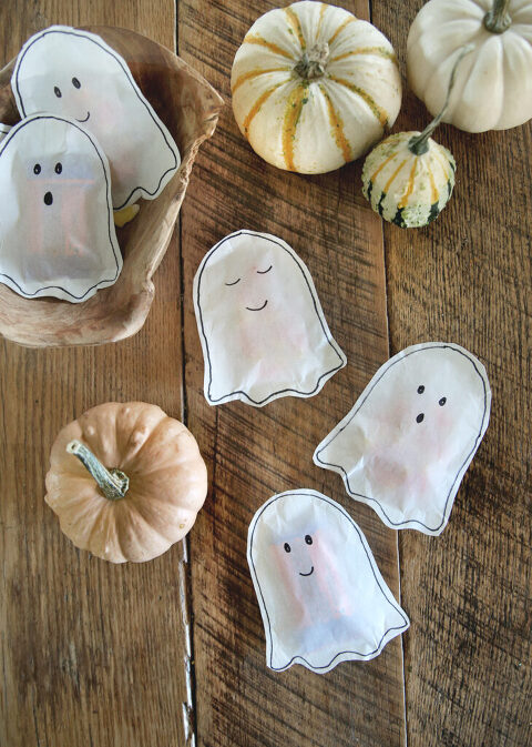 white paper ghost treat tons laying on wood table with small pumpkins surrounding