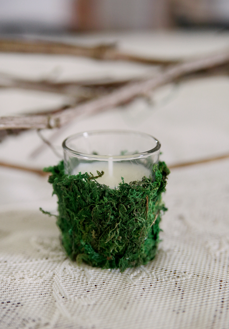 moss wrapped candle sitting on white lace tablecloth with vines behind it