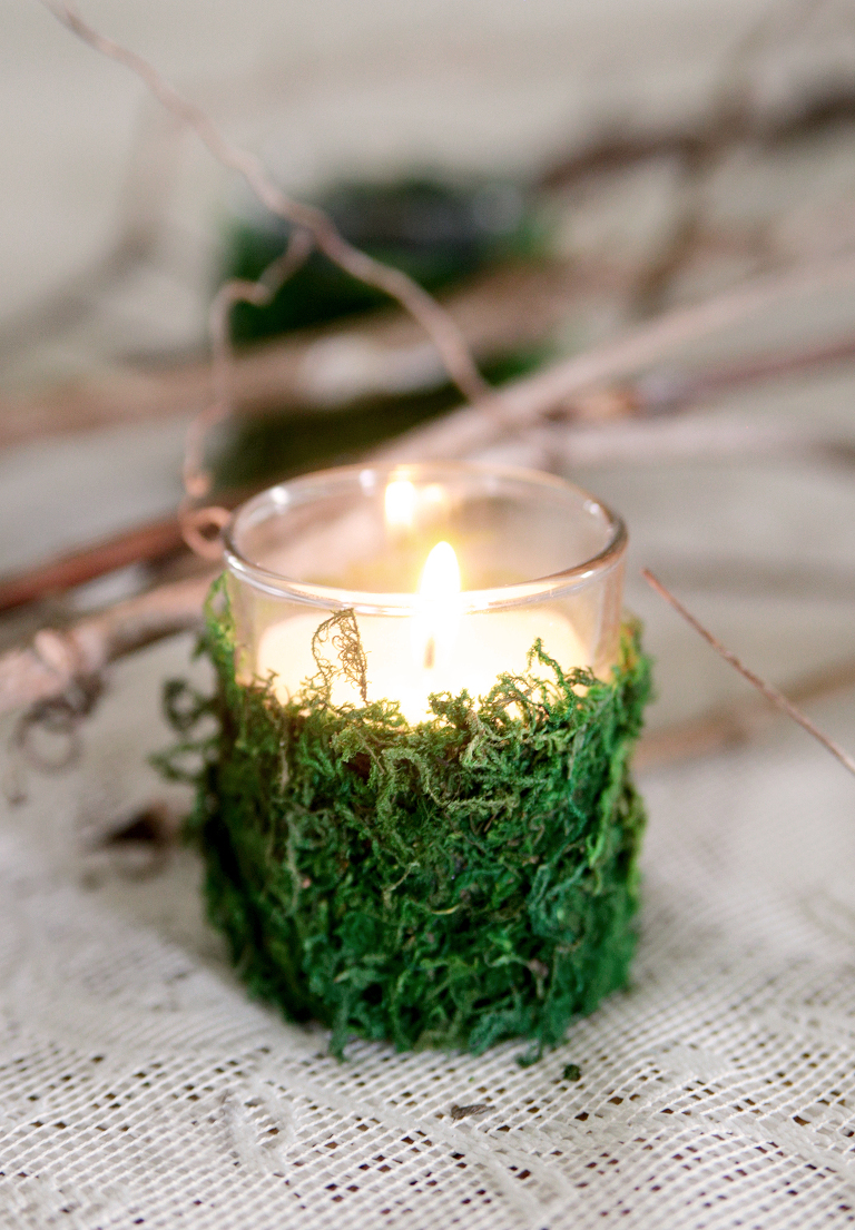 green moss votive candle sitting on lace tablecloth with vines behind it