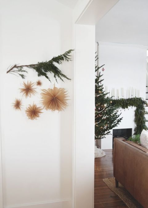 greenery branch with paper stars hanging from it on white wall