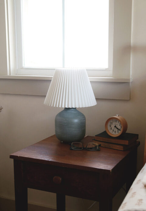 wood night stand with a vase lamp on it with a white pleated shade