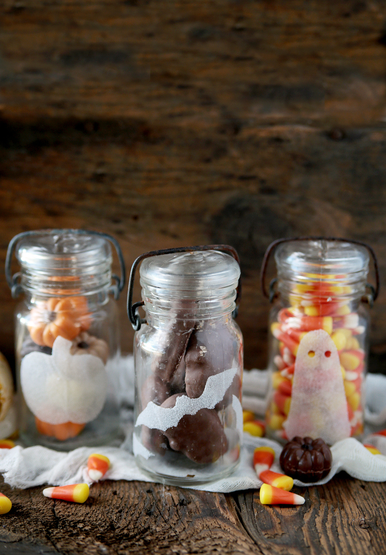 3 vintage glass jars with halloween salt stickers on them sitting on wood board with halloween candy in the jars