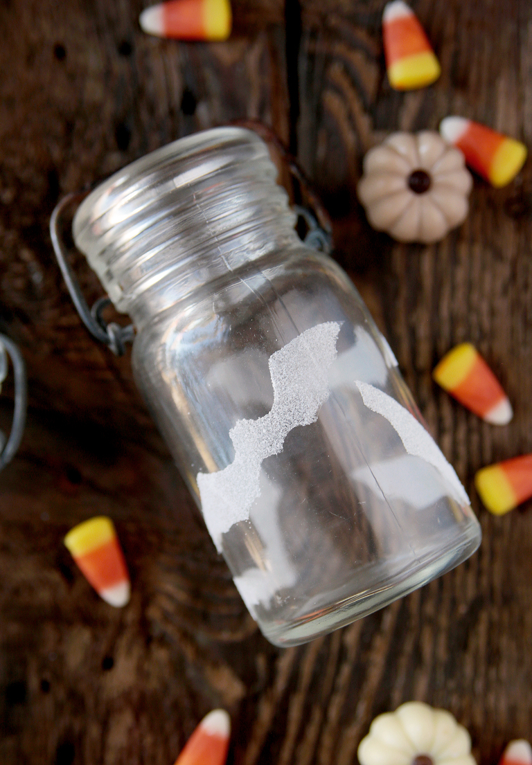 glass jar with salt bat stickers on it laying on wood board with candy corn and candy pumpkins around jar