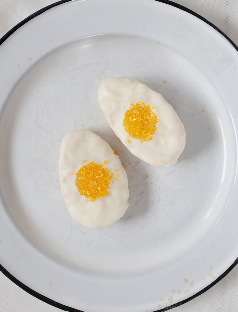 two egg shaped rice krispie treats dipped in white chocolate with yellow sprinkles in the middle to look like eggs