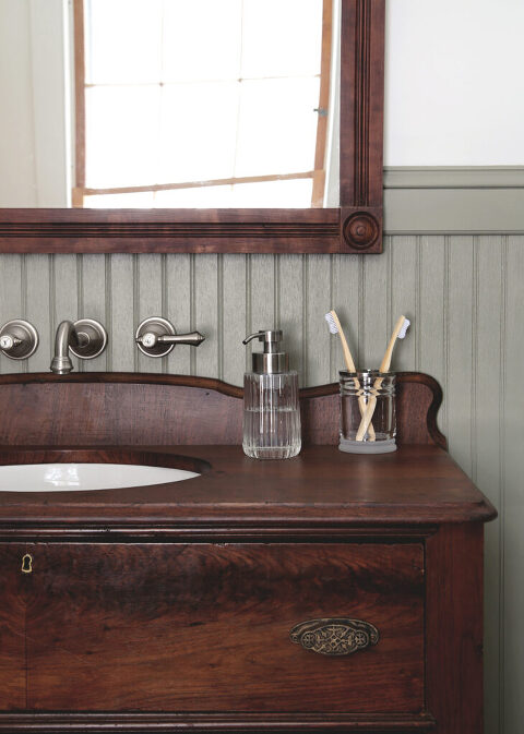 close up of vintage wood dresser bathroom sink vanity with glass soap dispenser and toothbrush holder on it