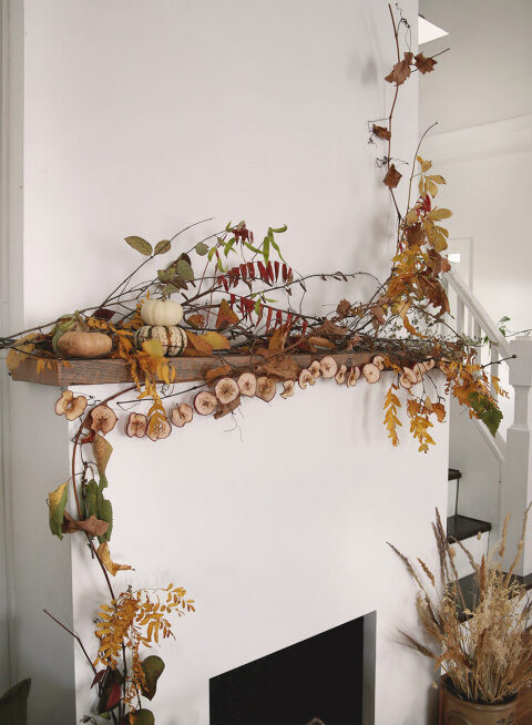 fireplace with wood mantel with fall leaves and branches with dried apple garland hanging mantel and pumpkins on mantel