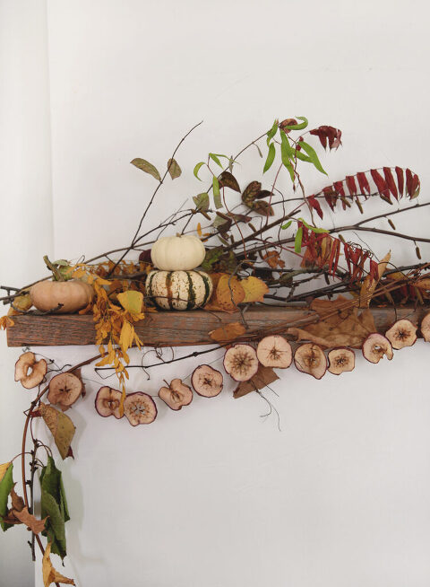 wood mantel with fall leaves and branches on it with a dried apple garland and pumpkins