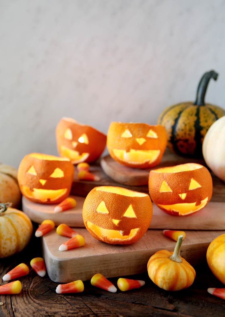 dried orange jack-o'-lanterns with beeswax tea light candles in them sitting on wood cutting boards with candy and mini pumpkins around them