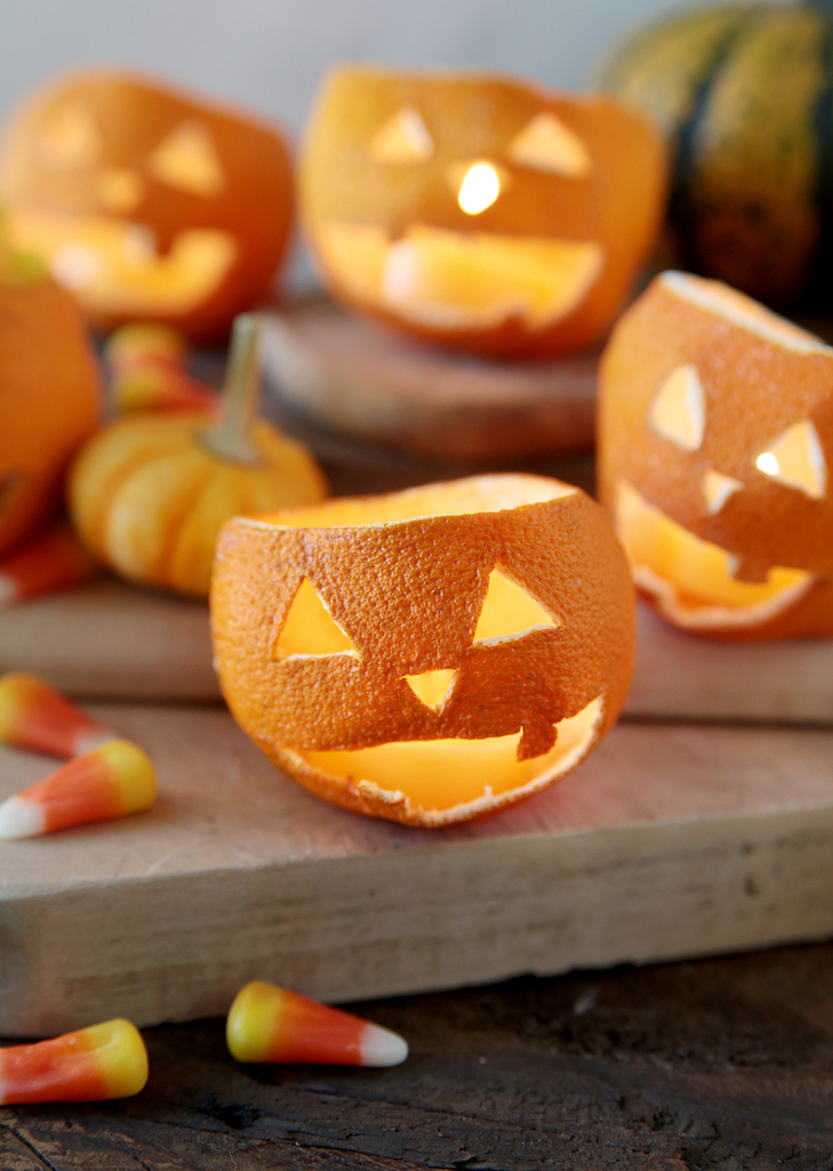 dried orange jack-o'-lanterns with beeswax tea light candles in them sitting on wood cutting boards with candy and mini pumpkins around them