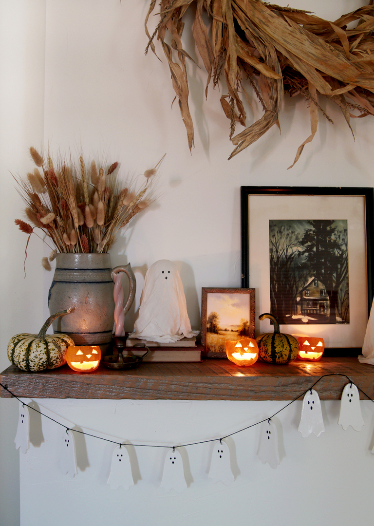 wood mantel decorated for halloween with ghosts and mini pumpkins and dried orange jack o lanterns