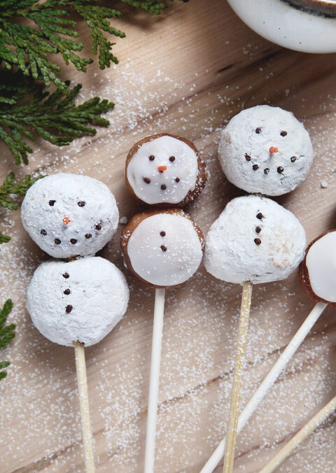 3 donut slum snowman on skewers laying on wood wearing workbench with sprinkle faces
