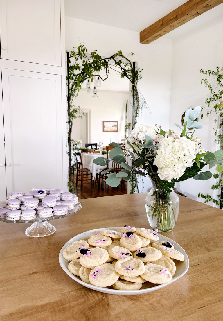 tray of floral sugar cookies next to platter of lavender macarons and vase of flowers