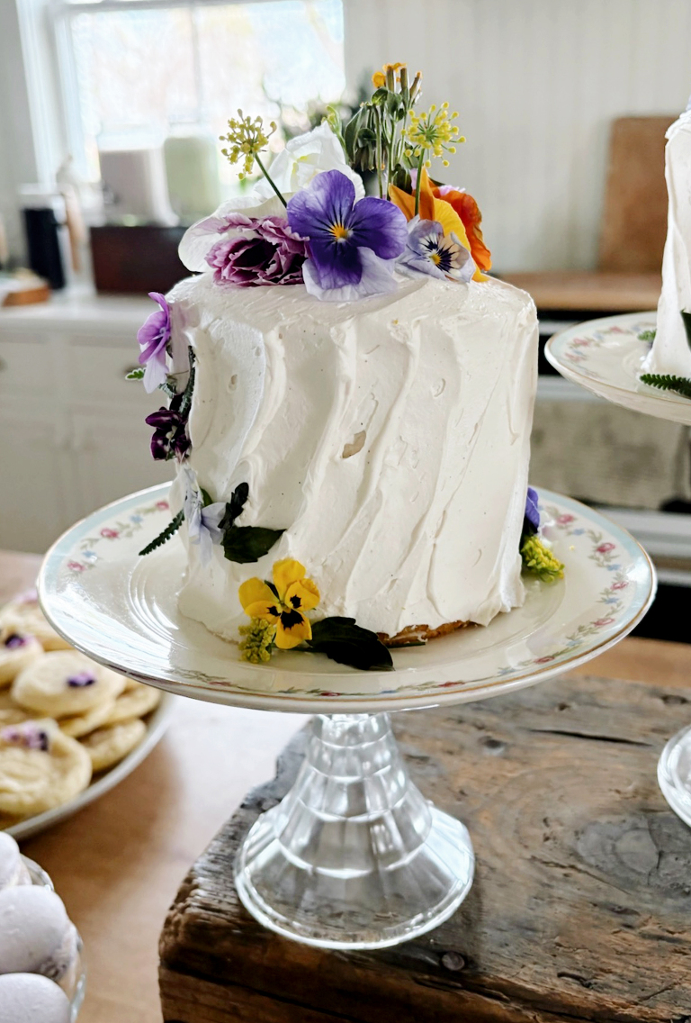 small cake decorated with edible flowers on vintage cake stand