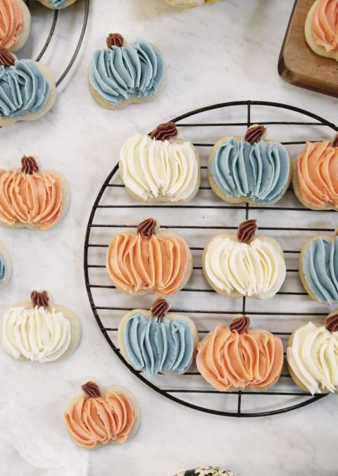 piped frosted pumpkin sugar cookies on round cooling rack