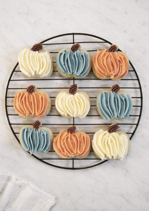 round cooling rack with pumpkin sugar cookies on it frosted in orange, white and blue frosting