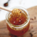 jar of honey with red pepper flakes in it with wood honey stick lifting out honey
