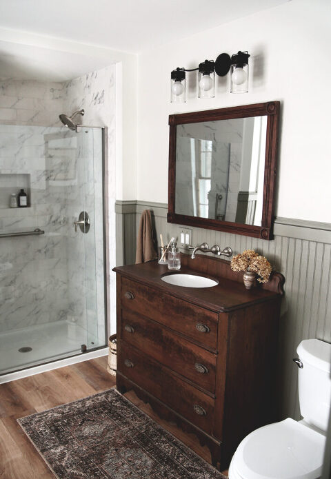 bathroom with beadboard walls and dresser sink vanity with wood framed mirror hanging whilom it
