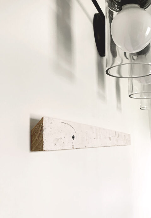 wood french cleat attached to white wall with lights above it