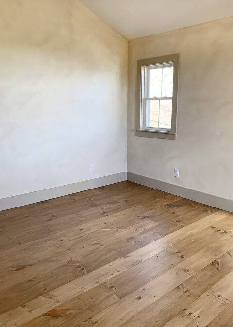 bedroom with beige limewash walls and stained pine floors installed