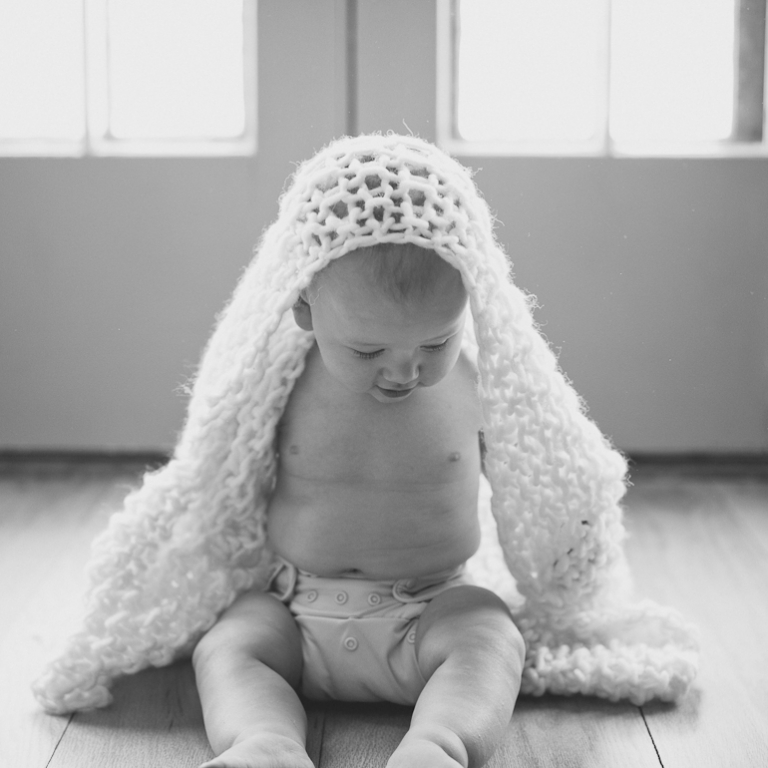 black and white photo of baby boy with chunky knit blanket wrapped around him