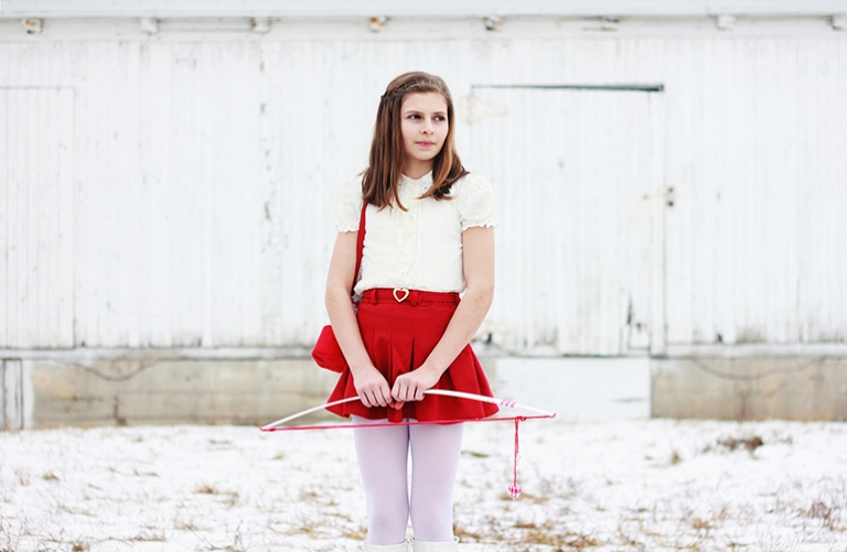 girl in front of white barn holding valentine's day bow