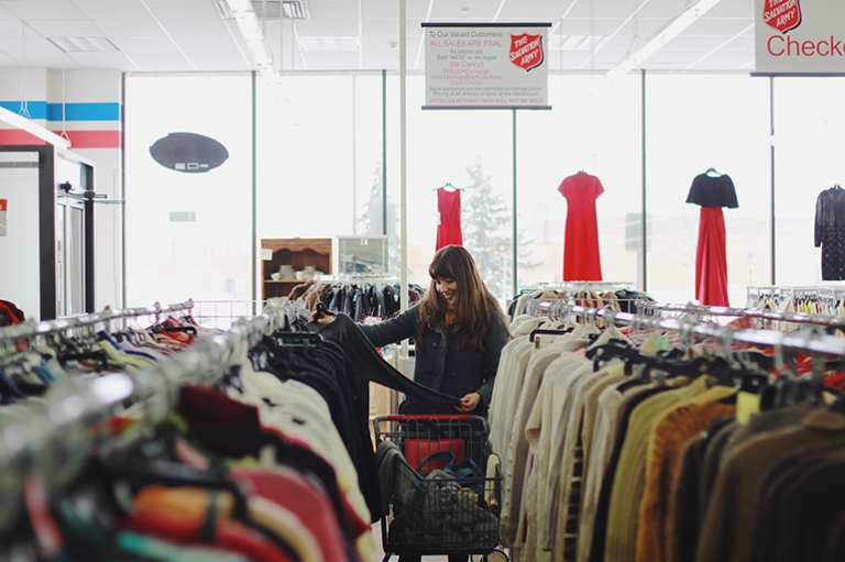 woman in thrift store aisle holding out a shirt