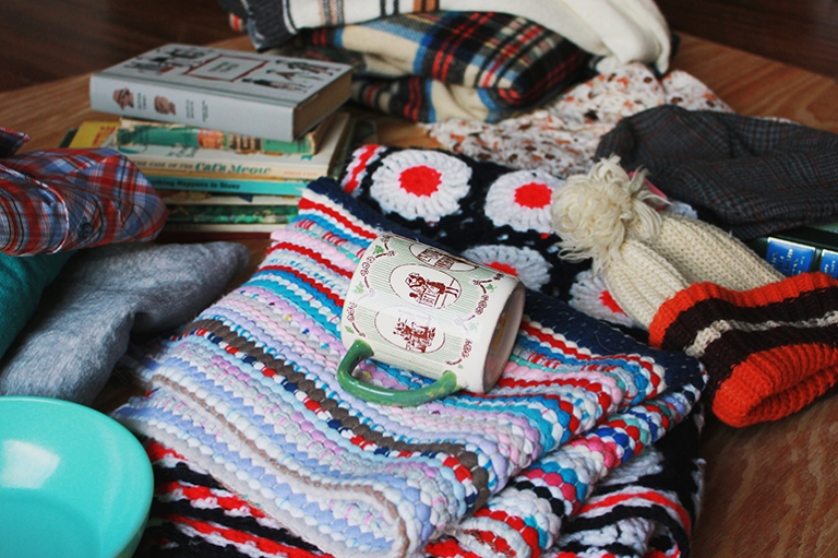 pile of thrifted purchases, books, blankets, and a mug