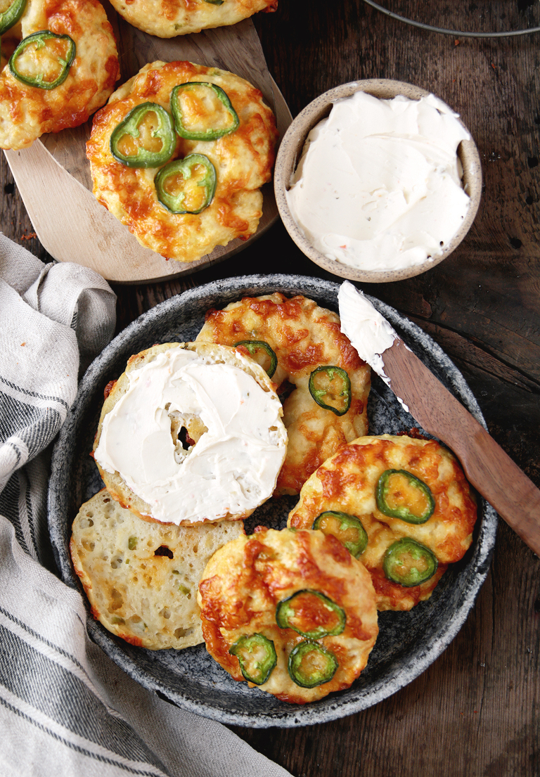 metal pie plate filled with bagels, with one bagel cut with cream cheese spread on bagel