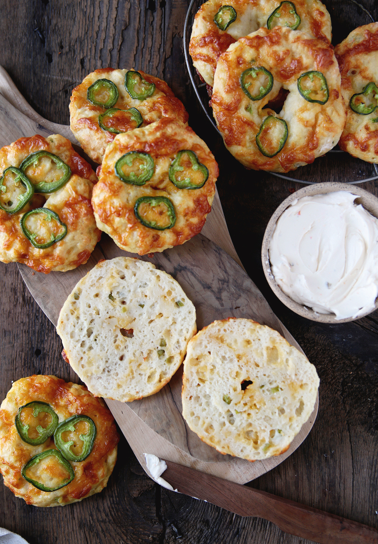 cut bagel on cutting board next to cheddar jalapeno bagels and bowl of cream cheese on wood counter