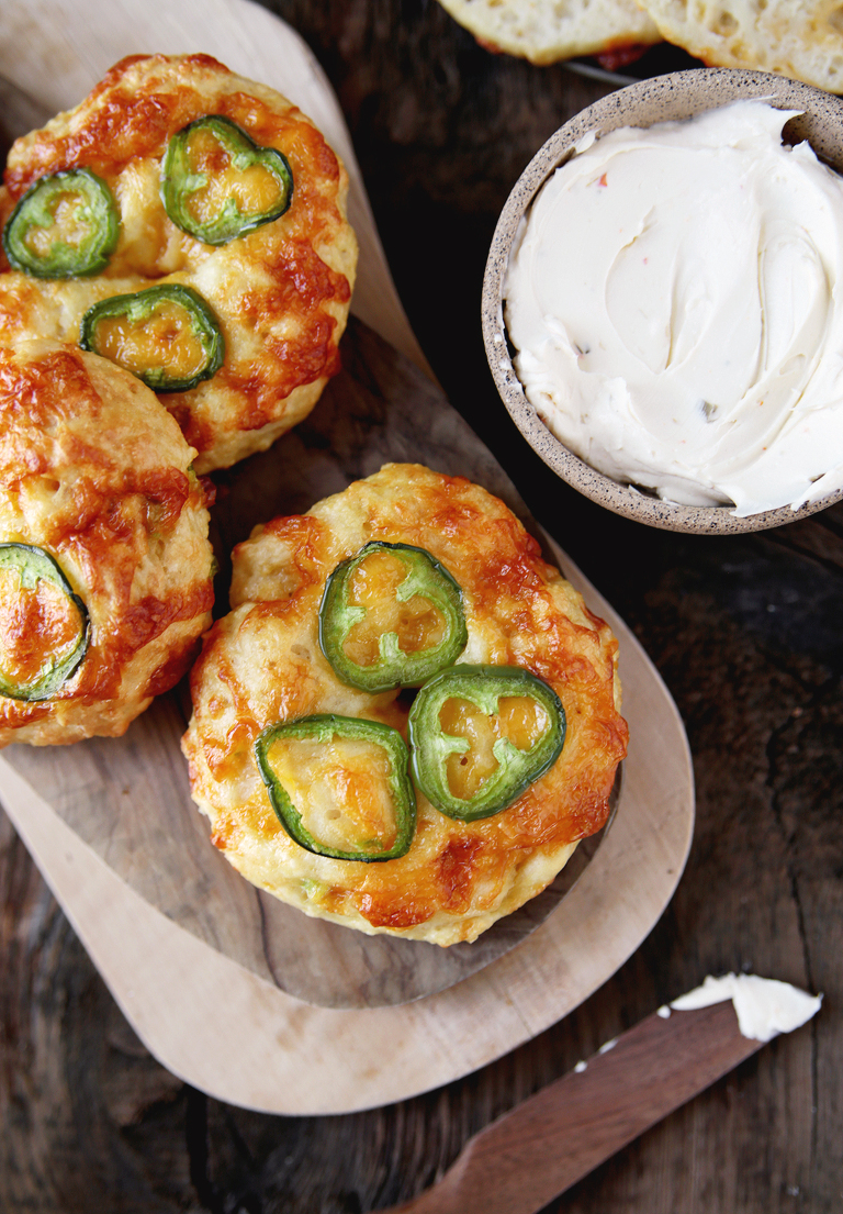 wood cutting board with cheddar jalapeno bagels on it next to bowl of cream cheese and wood knife