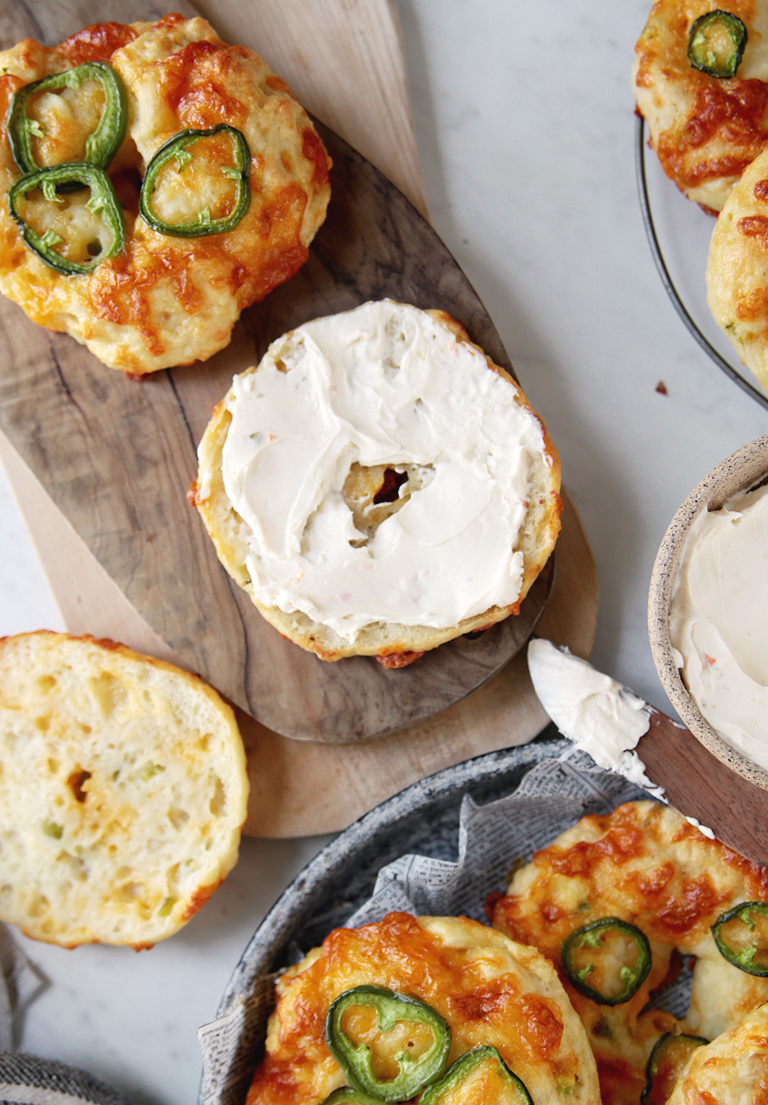 wood cutting board with cut bagel on it with cream cheese spread on bagel