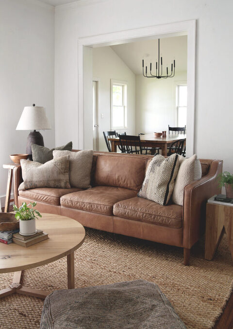 living room with brown leather couch with throw pillows on it and jute rug
