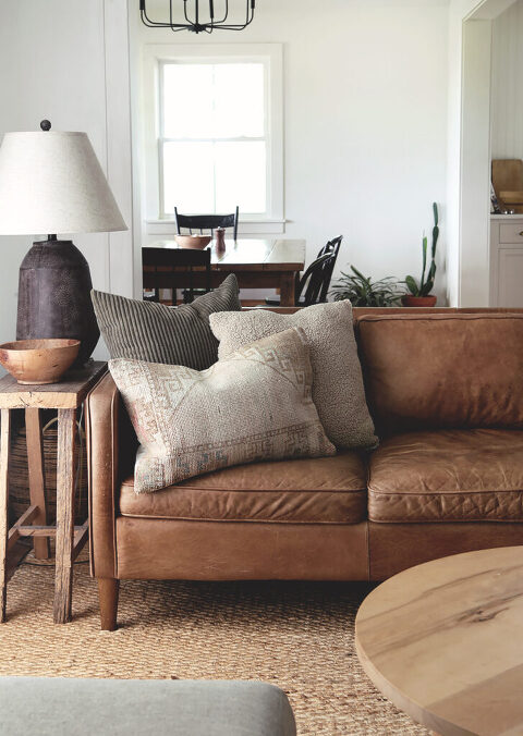 living room with brown leather hovel with throw pillows on it with lamp on end table next to couch