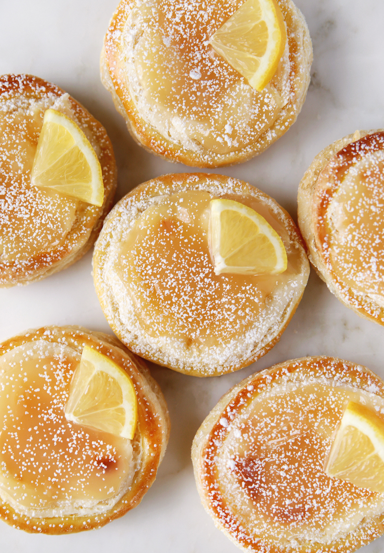 six lemon danishes with powdered sugar and lemon wedge topping pushed together