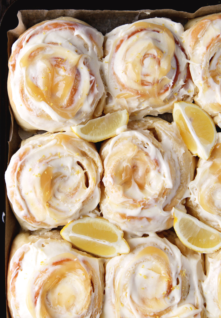 overhead shot of frosted sweet rolls on cookie sheet with lemon wedges in between rolls