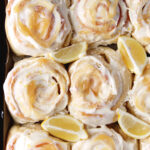 overhead shot of frosted sweet rolls on cookie sheet with lemon wedges in between rolls