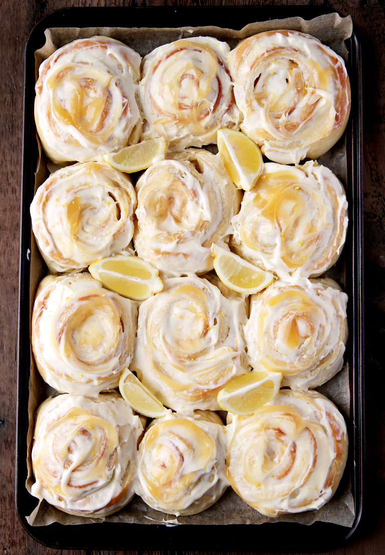 overhead shot of 12 frosted lemon sweet rolls on cookie sheet with lemon wedges in between rolls