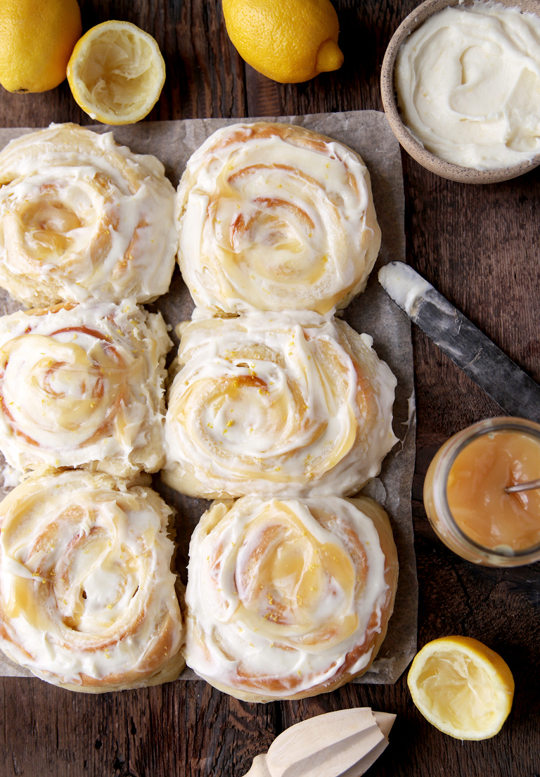 overhead shot of 6 rolls on wood board with lemons, frosting and lemon curd surrounding rolls