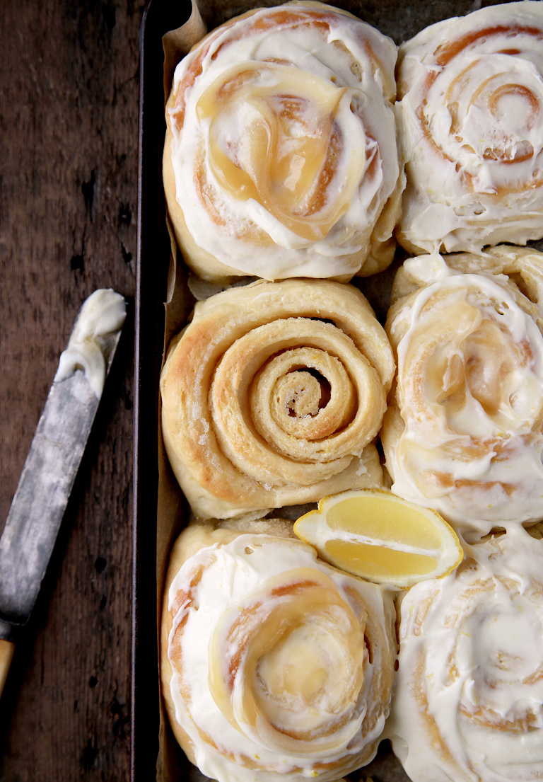 lemon rolls on cookie sheet with one roll unfrosted and lemon wedge in between rolls