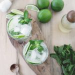 cutting board with drinks on it and lime mint simple syrup in bottle with limes and mint around it