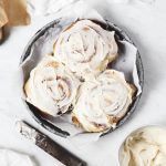round pan of three cinnamon rolls next to knife with frosting