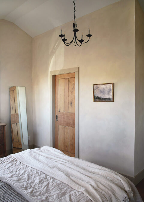 master bedroom with tan limewash walls with black chandlier hanging from vaulted ceiling and old wood