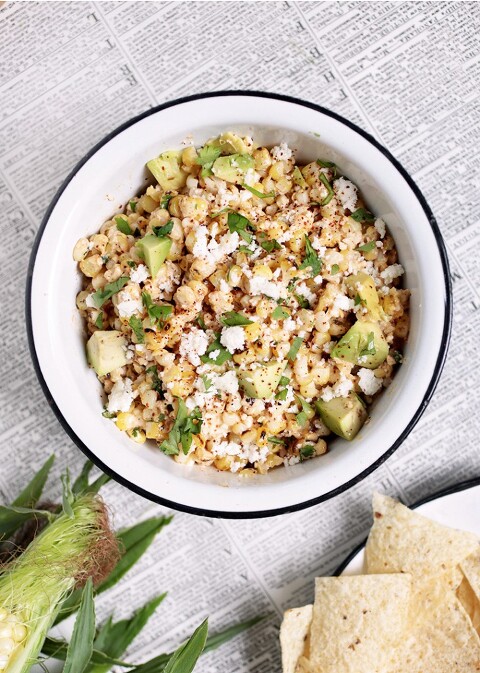 bowl of mexican street corn on newsprint with tortilla chips by bowl