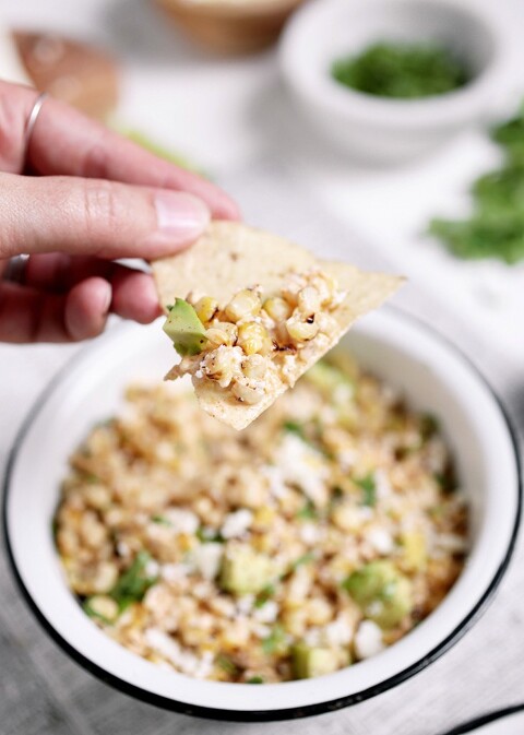 tortilla chip with mexican corn dip on it being scooped from bowl