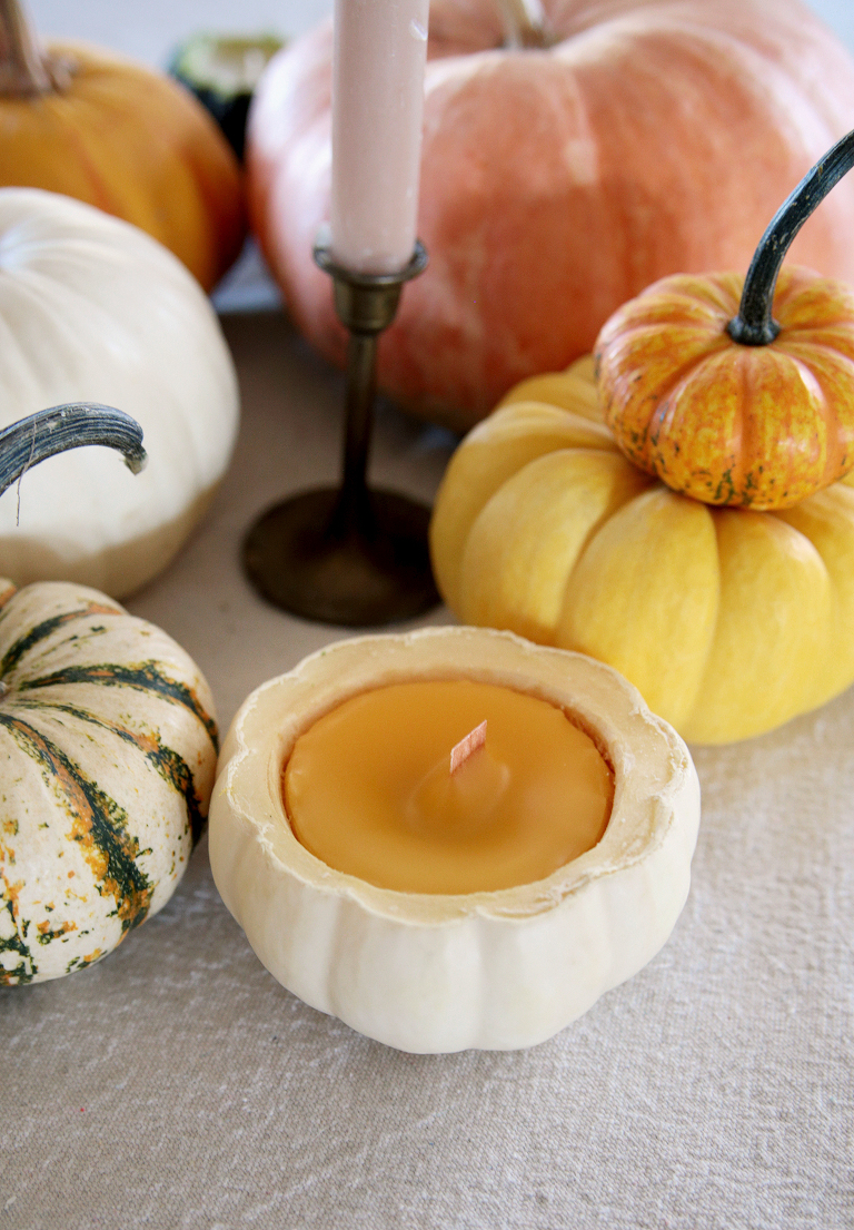 mini white pumpkin with yellow beeswax candle poured into it sitting on table next to pumpkins