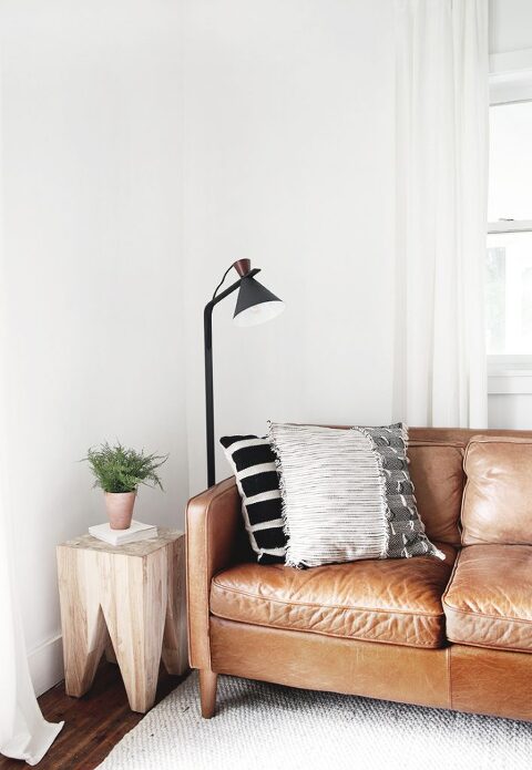 brown leather couch next to black lamp and wood side table