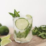 mojito mocktail in glass on wood cutting board with lime and mint around it